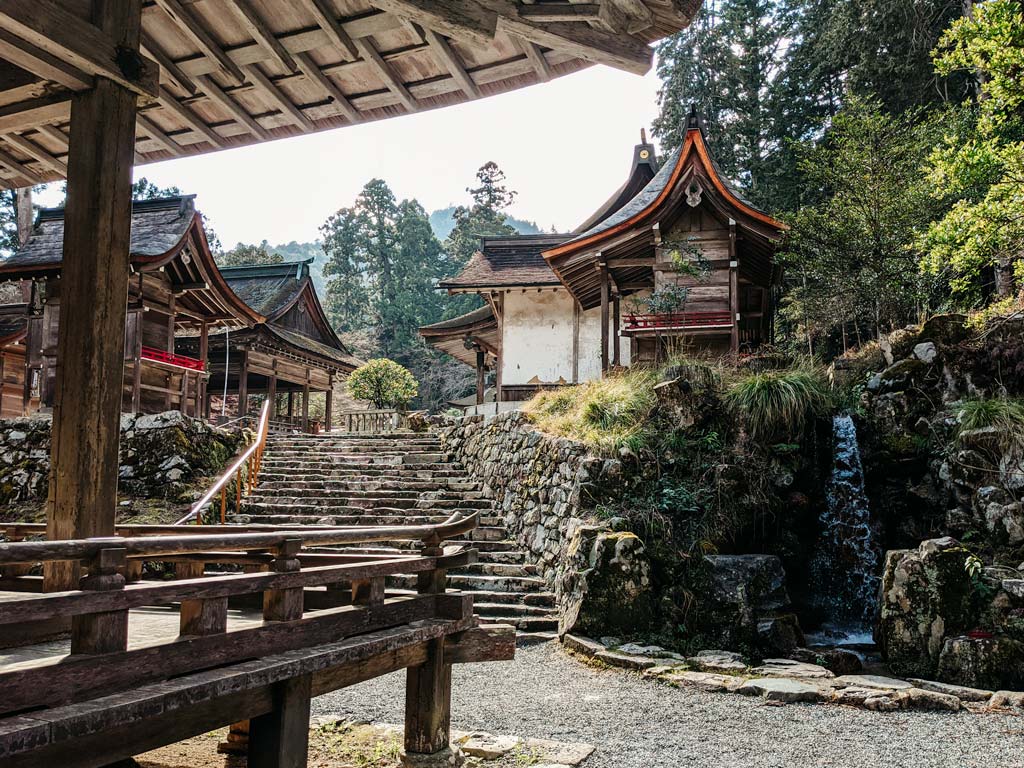 View of old wooden shrine buildings and small waterfall insdie Hiyoshi Taisha shrine complex.