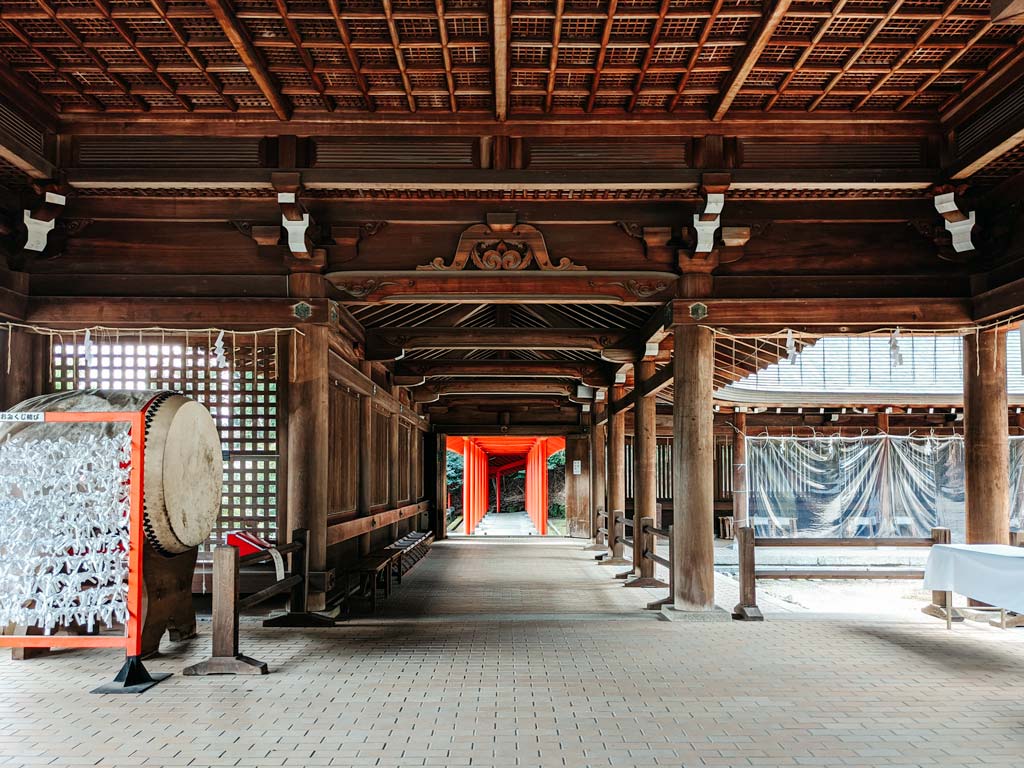 Interior of Omi-Jingu main hall with old drum, carved wooden ceiling, and view down torii gate path.