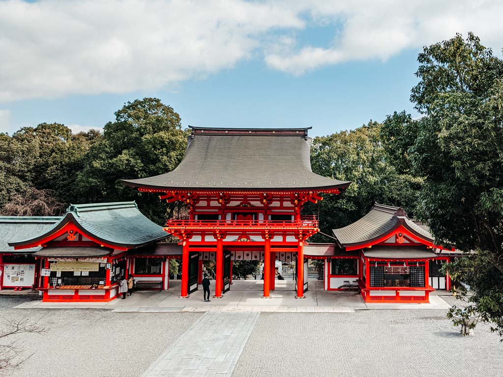 Vermillion and white gate of Omi-Jingu shrine with trees behind.