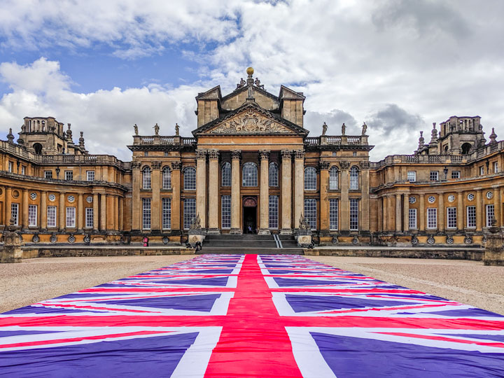 British flag walkway leading to Blenheim Palace entry with dozens of windows and columns.