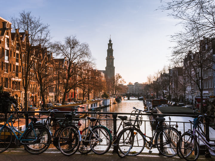 Sunset view of Amsterdam canal bridge with bikes against railing.