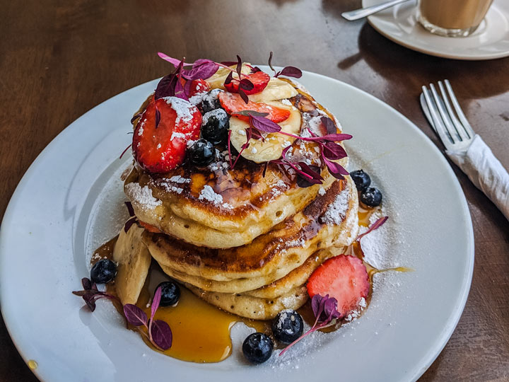 Stack of pancakes on white plate with berries and syrup.
