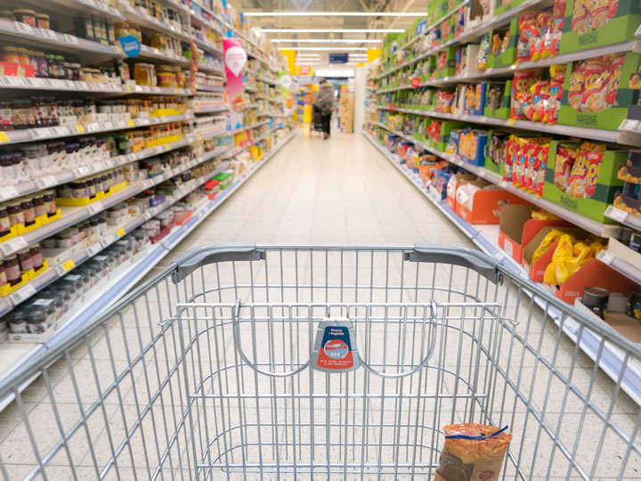 Shopping cart being pushed through grocery store aisle.