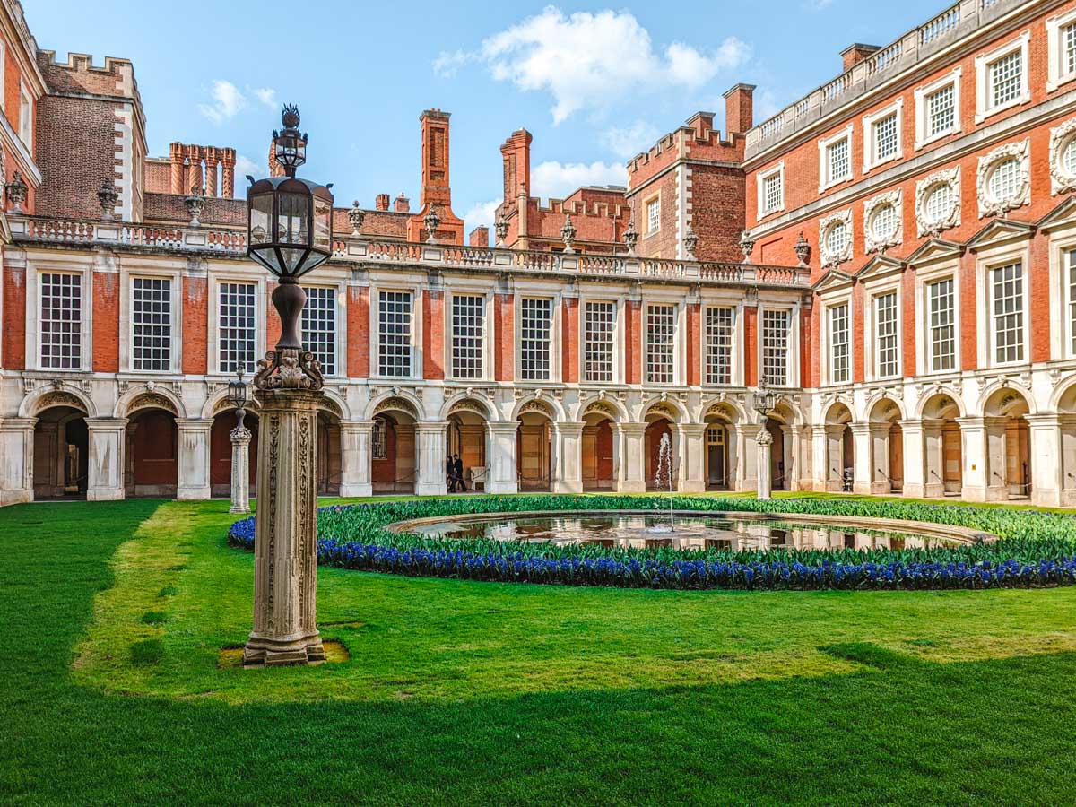 Interior courtyard of Hampton Court Palace with arched corridors and small pond.