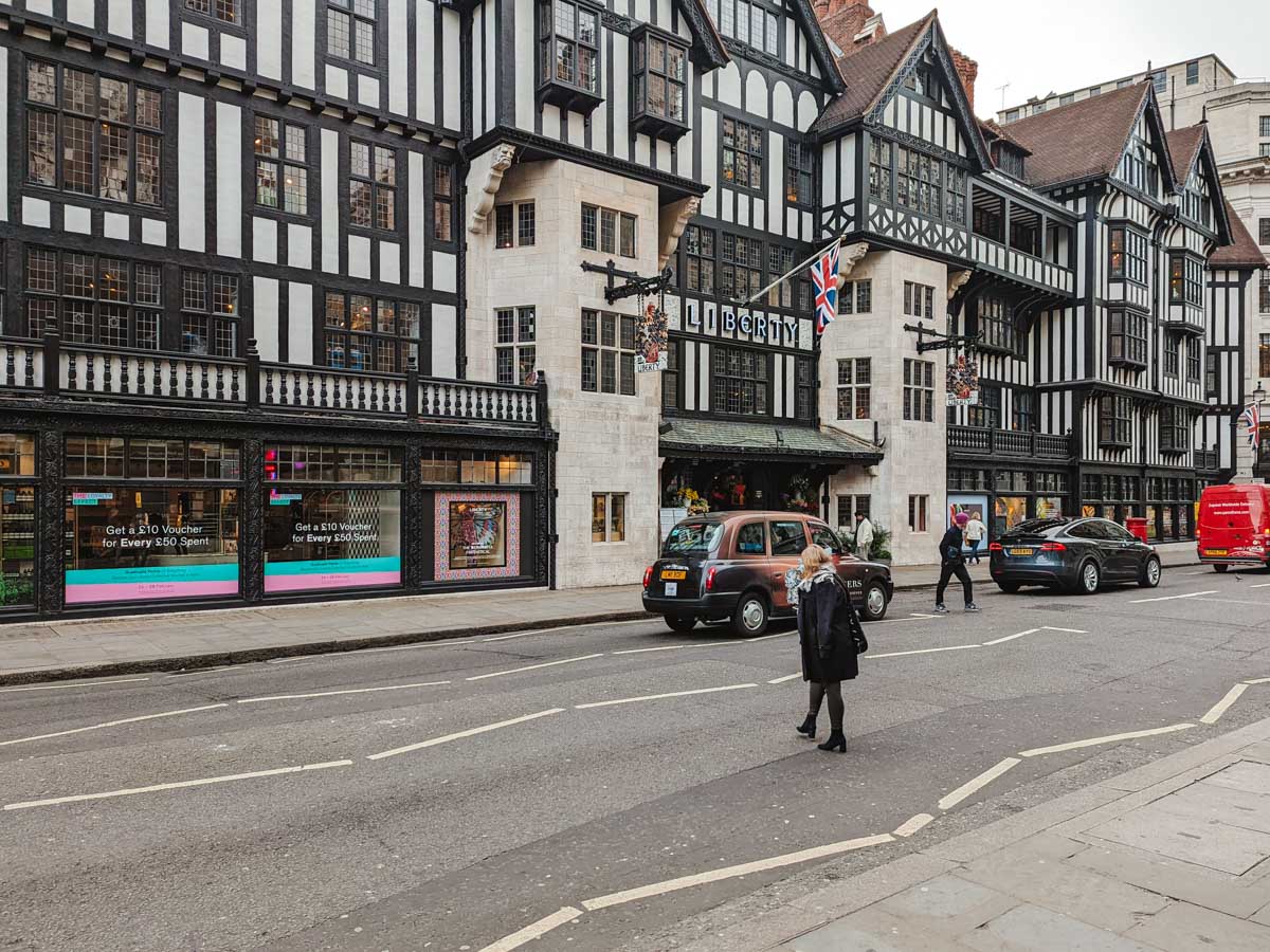 Half timbered black and white exterior of Liberty London department store with road in front.