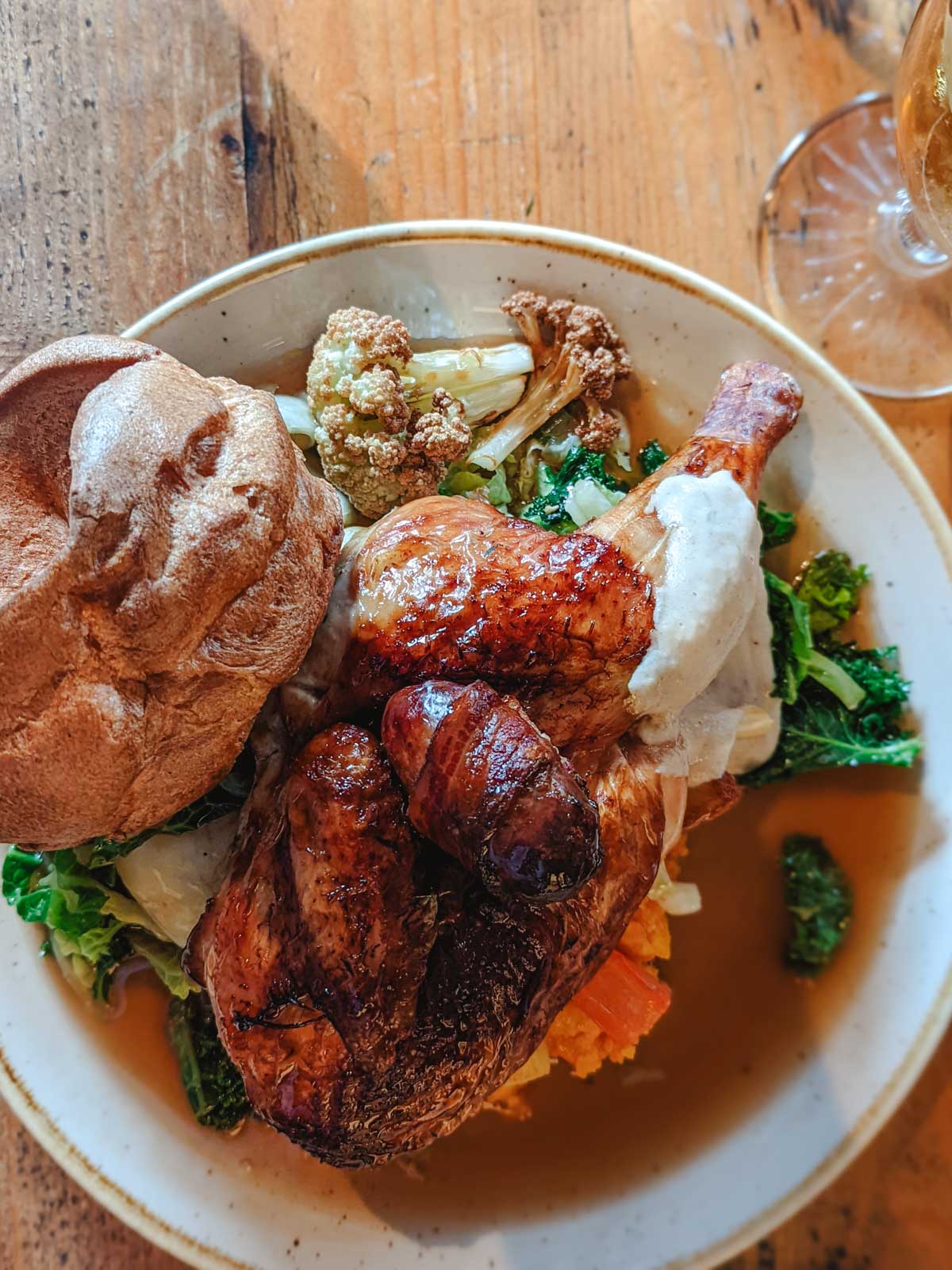 Plate of Sunday Roast with chicken leg, yorkshire pudding, gravy, greens, and cauliflower.