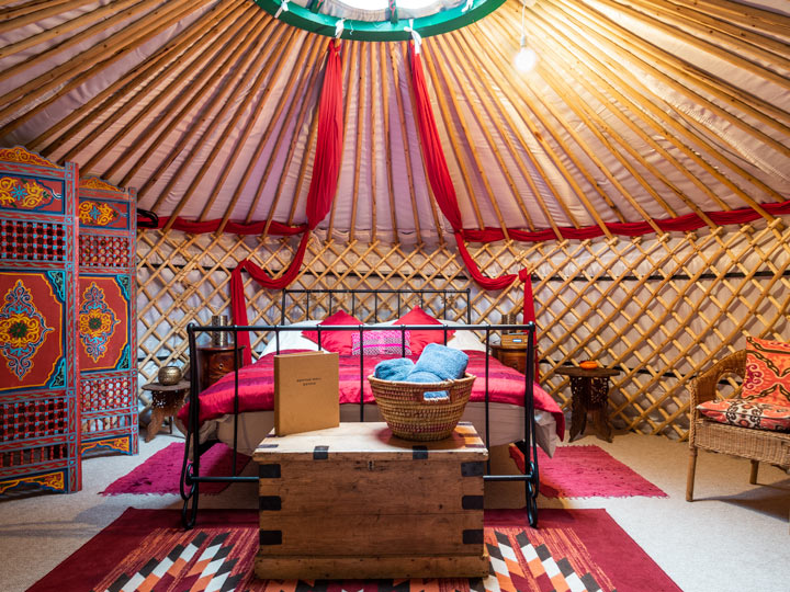 Luxury Glamping in Suffolk - Kenton Hall Estate yurt interior with red bed, chest, and screen.