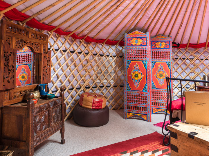 Glamping yurt interior with wooden dressing table, poufs, and screen.