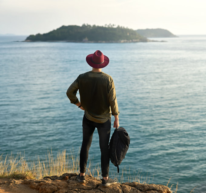 Man looking out at ocean holding the best minimalist travel backpack for carry on.