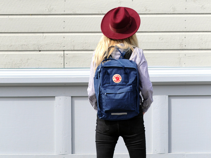 Woman wearing mix and match travel wardrobe of black jeans, red hat, and blue backpack.