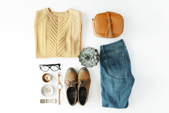 Flat lay of jeans, sweater, shoes, purse, and accessories.