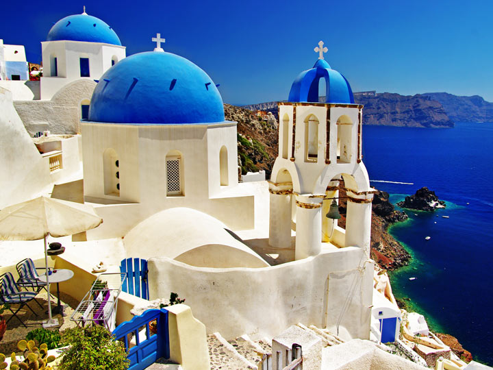 Whitewashed house with blue dome roofs overlooking ocean in Oia.