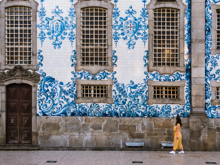 Girl in yellow dress walking past Porto church with blue and white azulejo tiles.