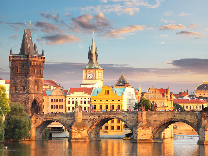 Sunrise over Prague bridge with gothic tower and houses in background.