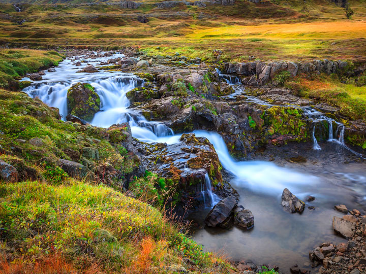 Iceland river waterfall with green and red grass surrounding pool.