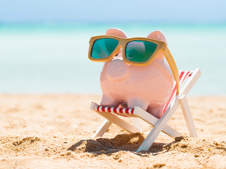 Piggybank wearing sunglasses sitting in beach chair on sand.