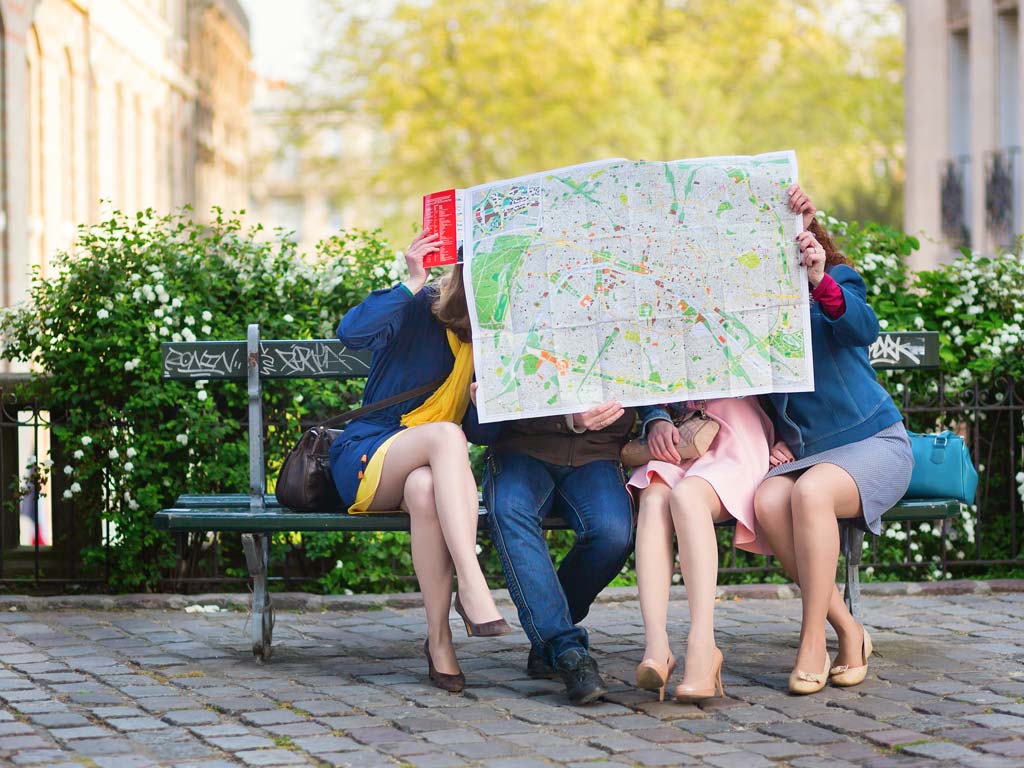 Four people living abroad in their 30s sitting on bench outside looking at large street map.