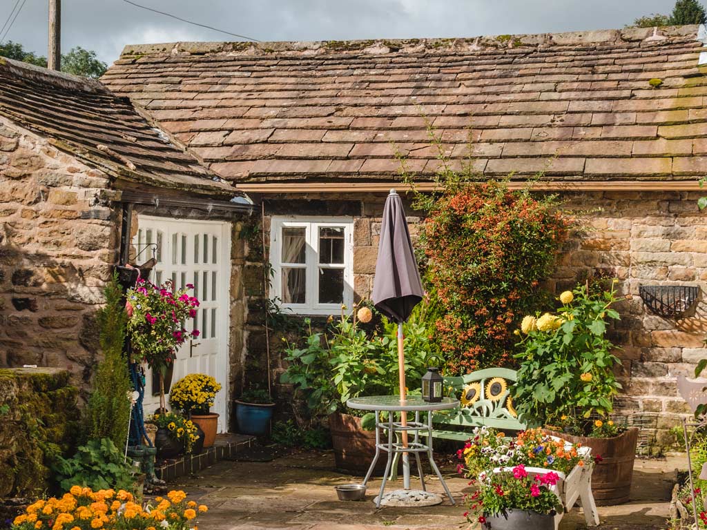 Small English stone cottage with patio garden covered in potted flowers.