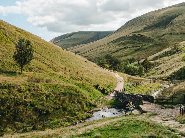 ruohoiset kumpuilevat kukkulat puroineen ja kivisiltoineen Peak District Englannissa