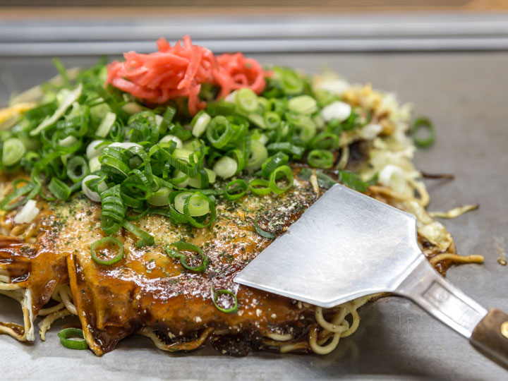 Okonomiyaki topped with negi and ginger on metal grill.