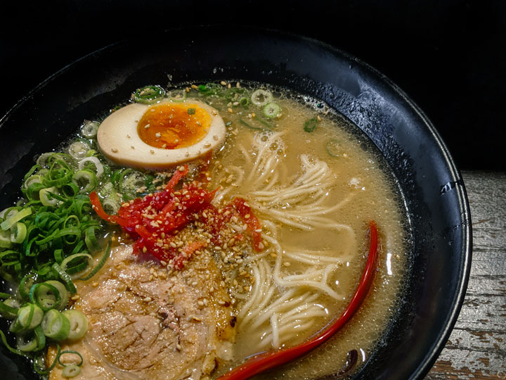 Black bowl of tonkotsu ramen with negi and onsen egg.