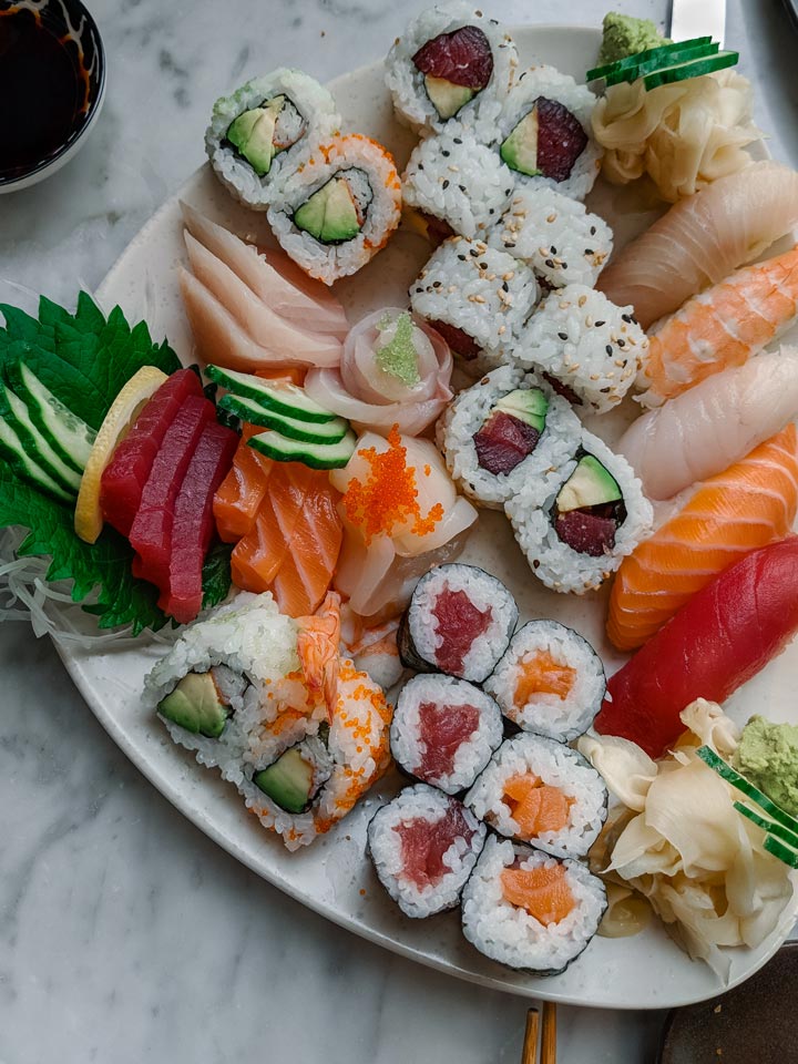 Platter of colorful sushi rolls, nigiri, and sashimi on white marble table.