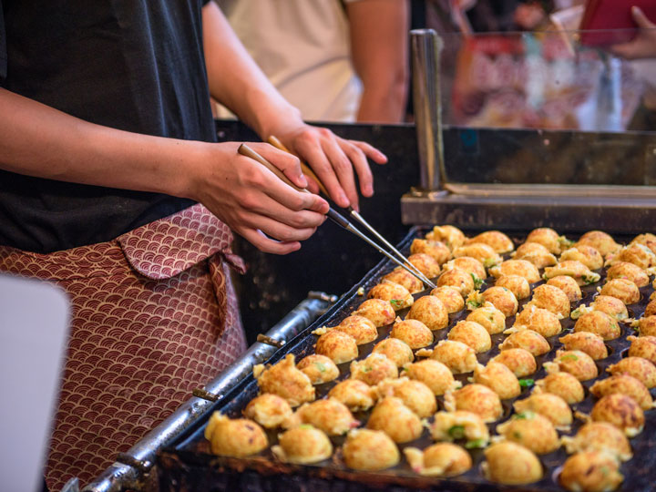 Man cooking takoyaki with pan at street food market.