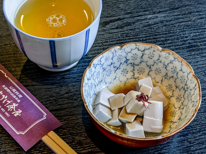 Purple tofu with dashi and tea in blue floral bowl next to chopsticks.