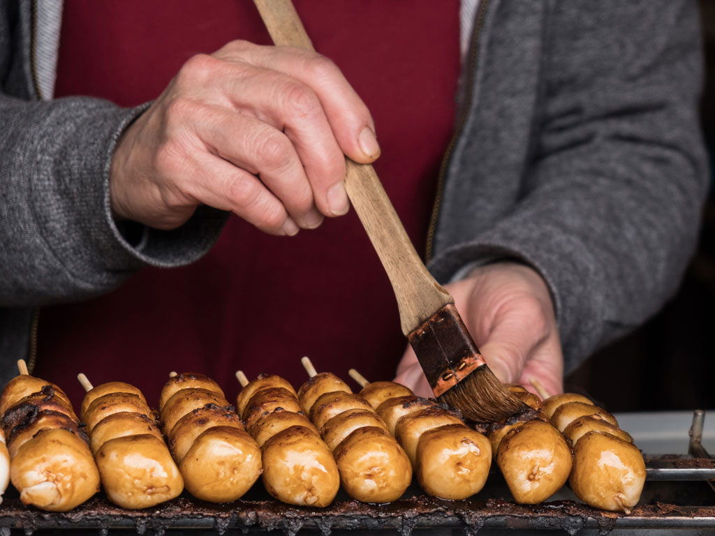 Man grilling dango and brushing skewers with sauce.