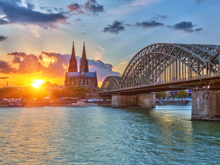 View of Hohenzollern Bridge over river with Cologne Cathedral and sunrise in background.