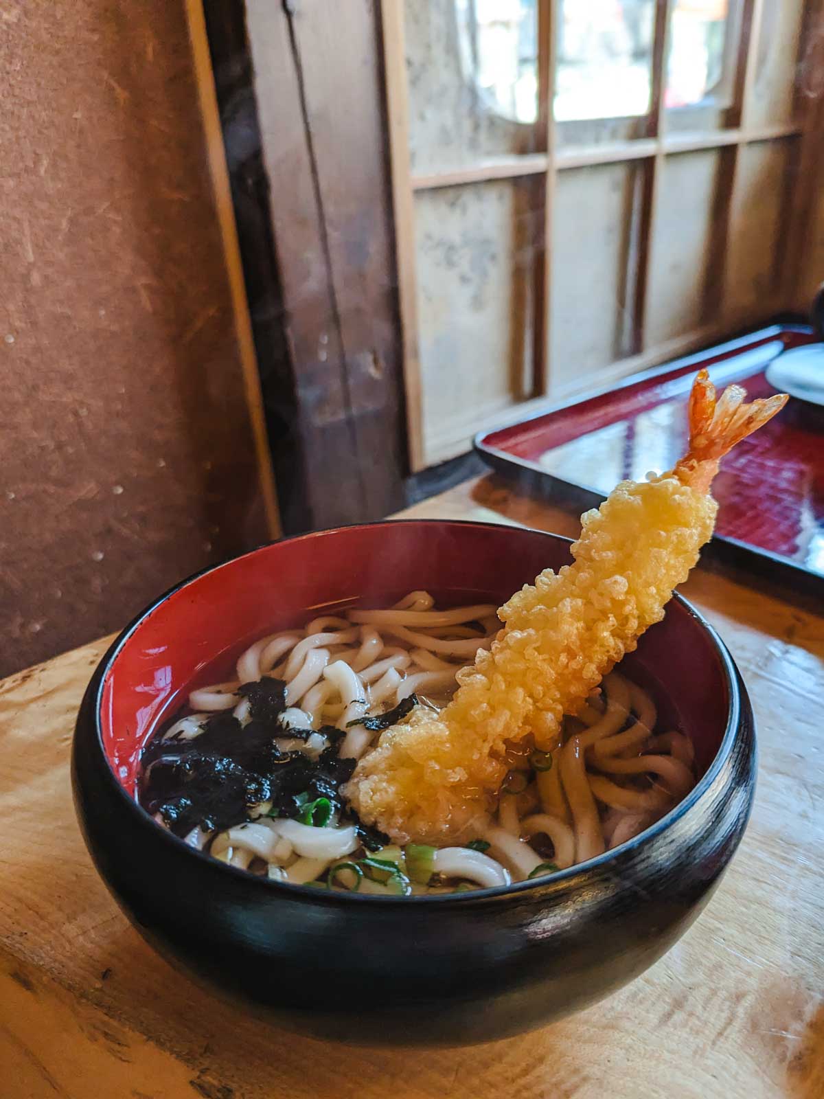 Bowl of tempura udon on wooden table.