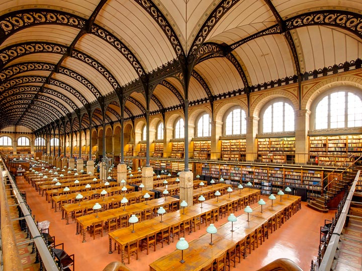Interior of reading room at Sainte-Genevieve library with long tables, bookshelves, and bright windows.