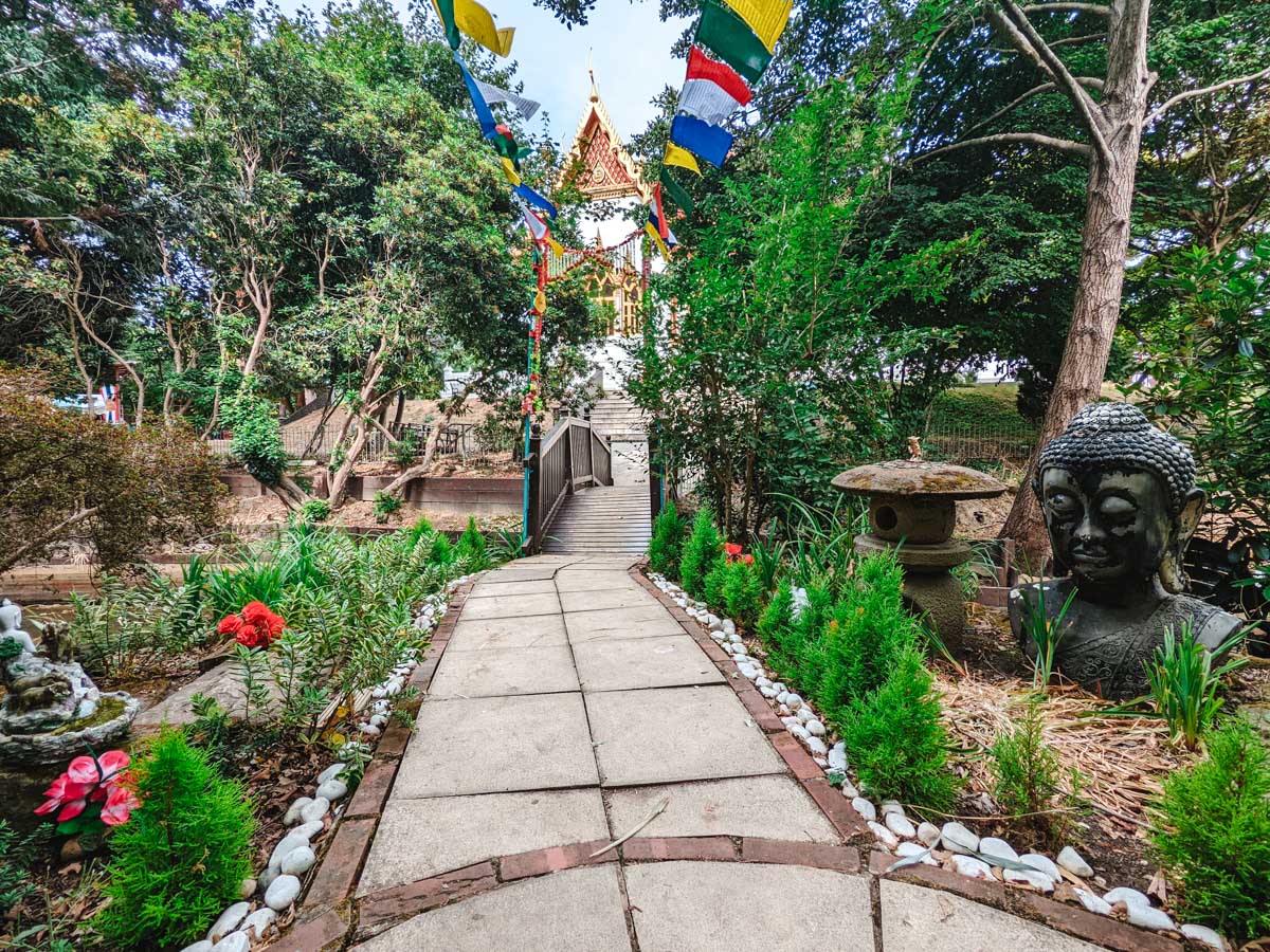Garden walking path at Buddhapadipa Temple with colored flags and Buddha statue.