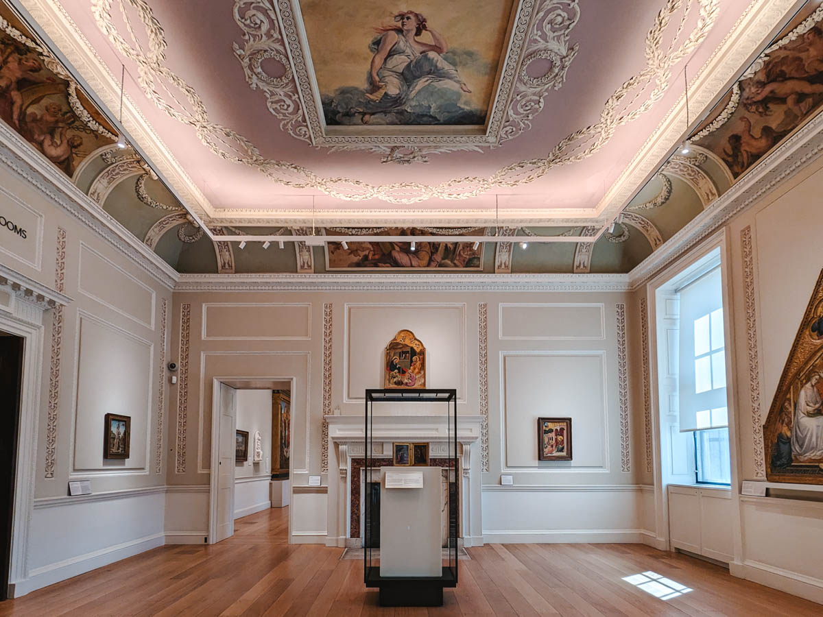 Interior of London's Courtauld Gallery with artwork on walls and fresco ceiling painting of woman.