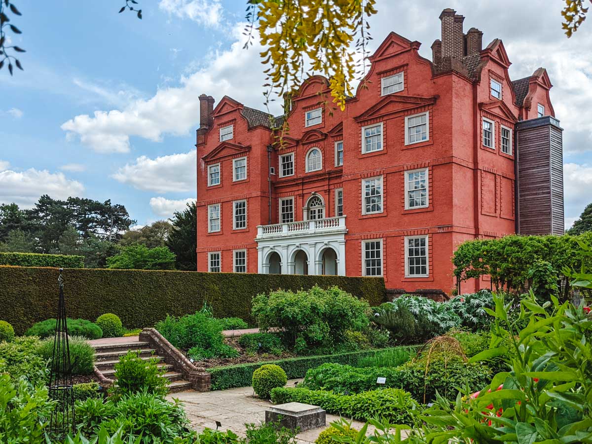 Red brick stately house in Kew Gardens with manicured walking paths in foreground.