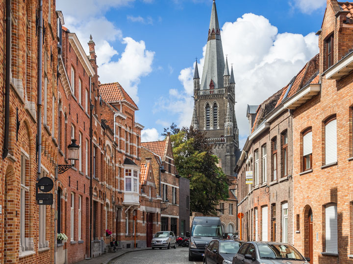 Street view of houses and distant cathedral viewed during one day in Bruges itinerary.