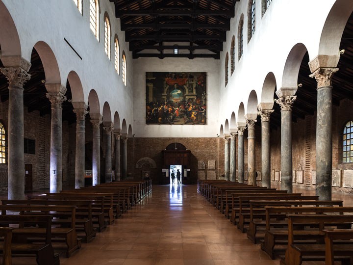 Interior aisle of Basilica di San Giovanni Evangelista with wooden benches and marble columns.