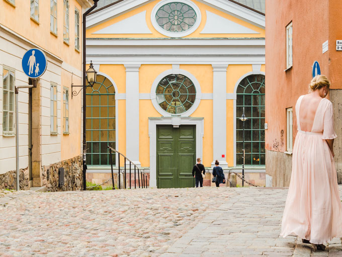 View of Katarina Kyrka yellow facade with woman wearing dress in foreground.