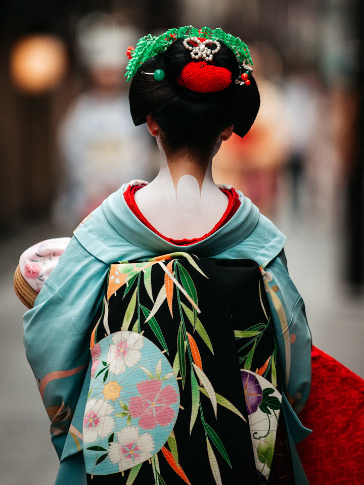 Geisha in blue kimono walking down street.