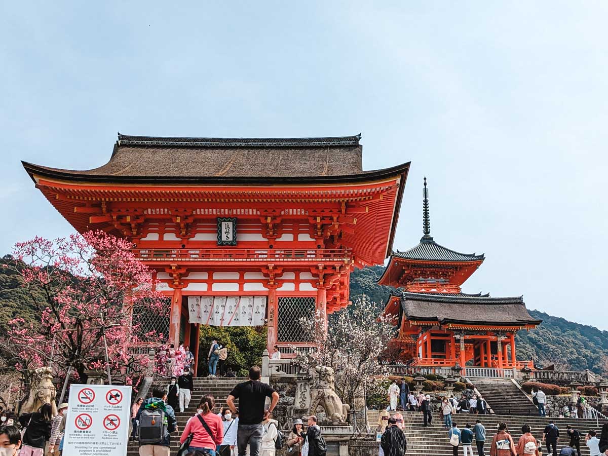 Stairs leading to main gate and small pagoda of Kiyomizudera with tourists in foreground.