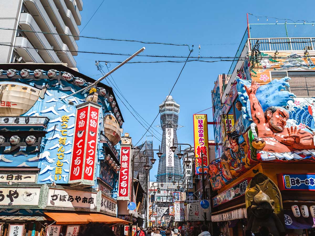Osaka Shinsekai Street with colorful buildings and Tsutenkaku radio tower in distance.