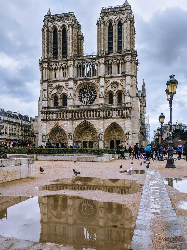 Exterior view of Notre Dame Cathedral on dark cloudy day with puddle reflection.