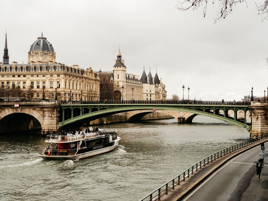 River boat traveling down Seine near green bridge.