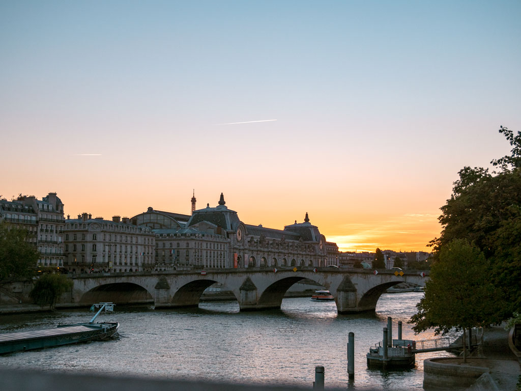 Sunset viewed from bridge over the Seine river with museum and bridge in distance.