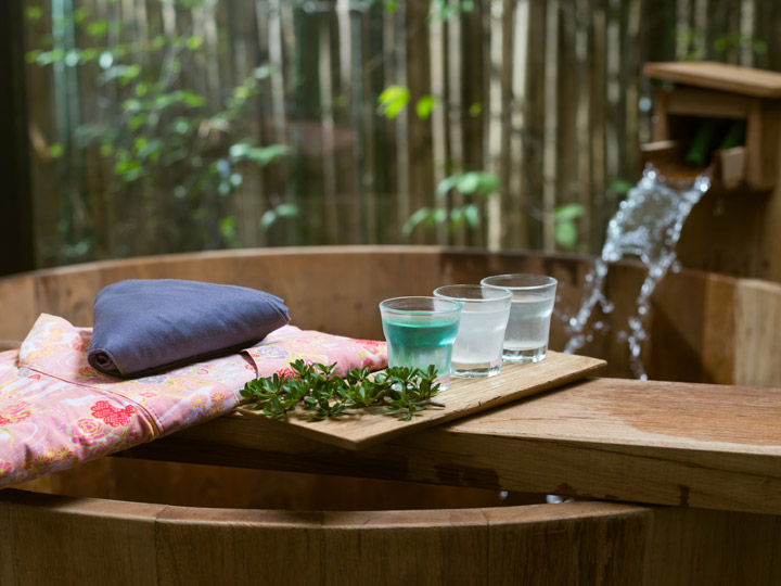 Atami onsen wooden bath with pink yukata and drinks on table.