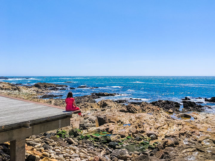 Girl in red dress sitting on Porto beach dock.