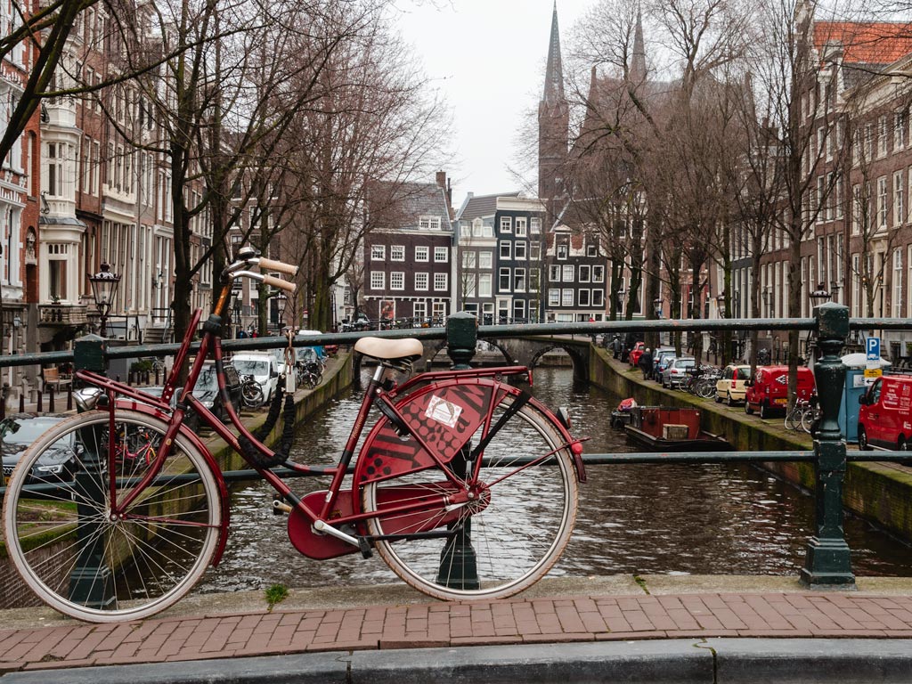 Red bicycle leaned against bridge railing over canal.