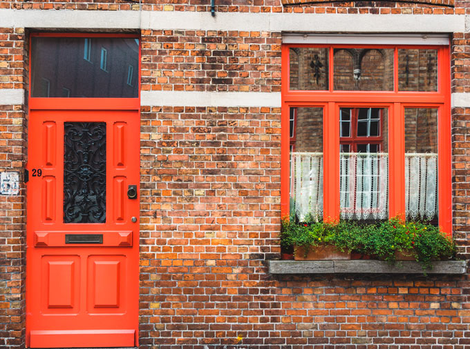 Facade of brick home with orange door and window, owned by person who wants to sell everything and start over.