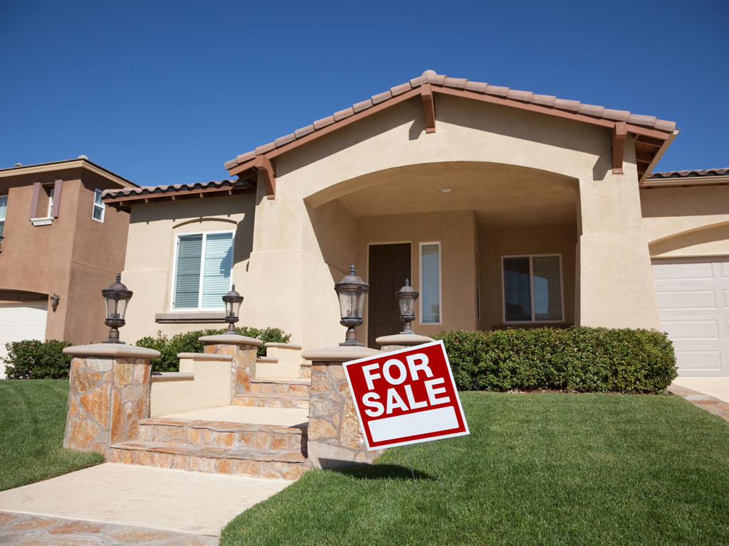 Exterior of front of house being sold before moving abroad, with "for sale" sign in yard.