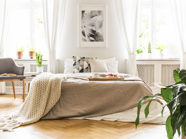 Light airy bedroom with grey bed, chair, and houseplant.